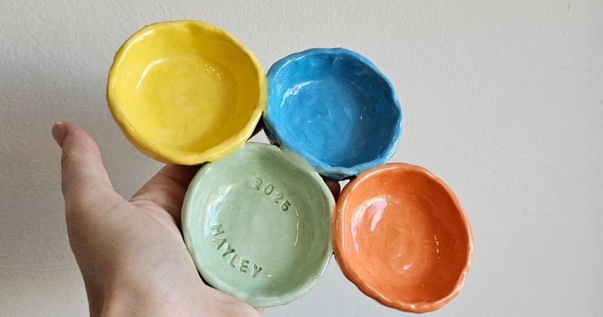 Closeup hand holding four glazed bowls in ceramic studio