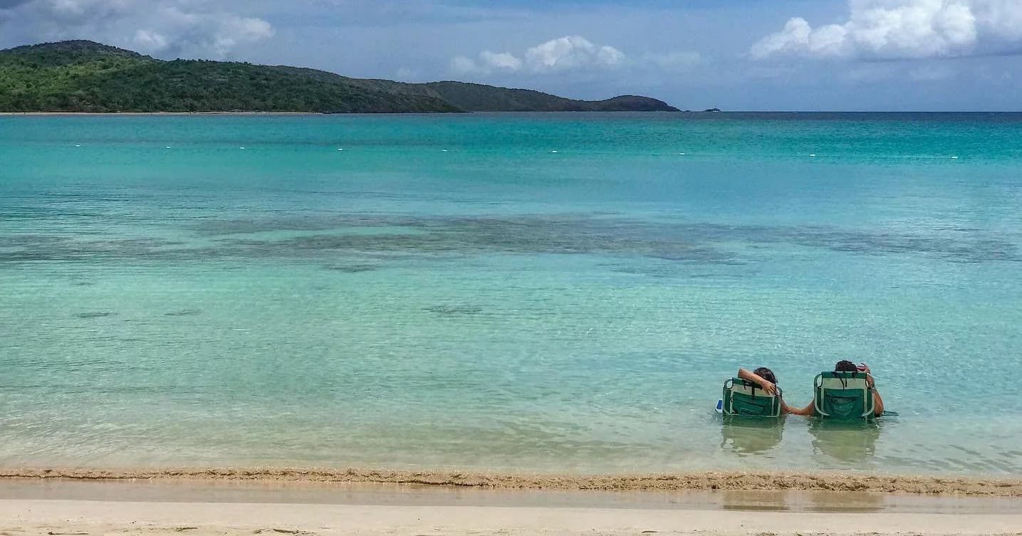 Empty beach chairs in shallow turquoise Caribbean bay at shore