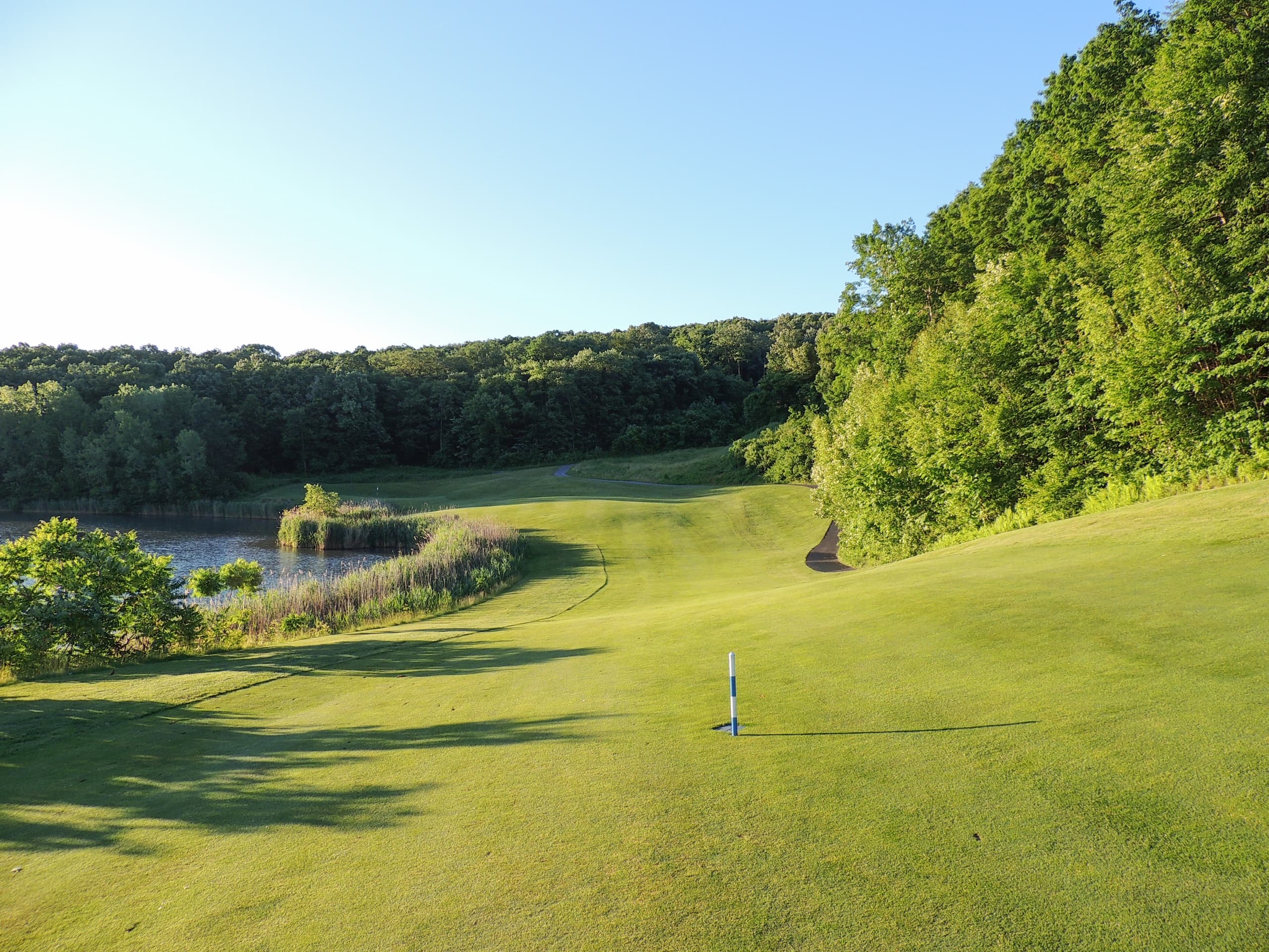 Golfer teeing from lakeside fairway on scenic forested golf course