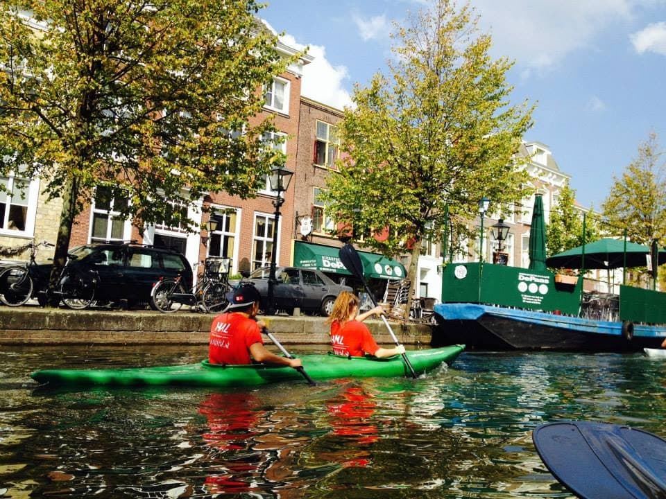 Two kayakers paddling past city houses on a sunny canal