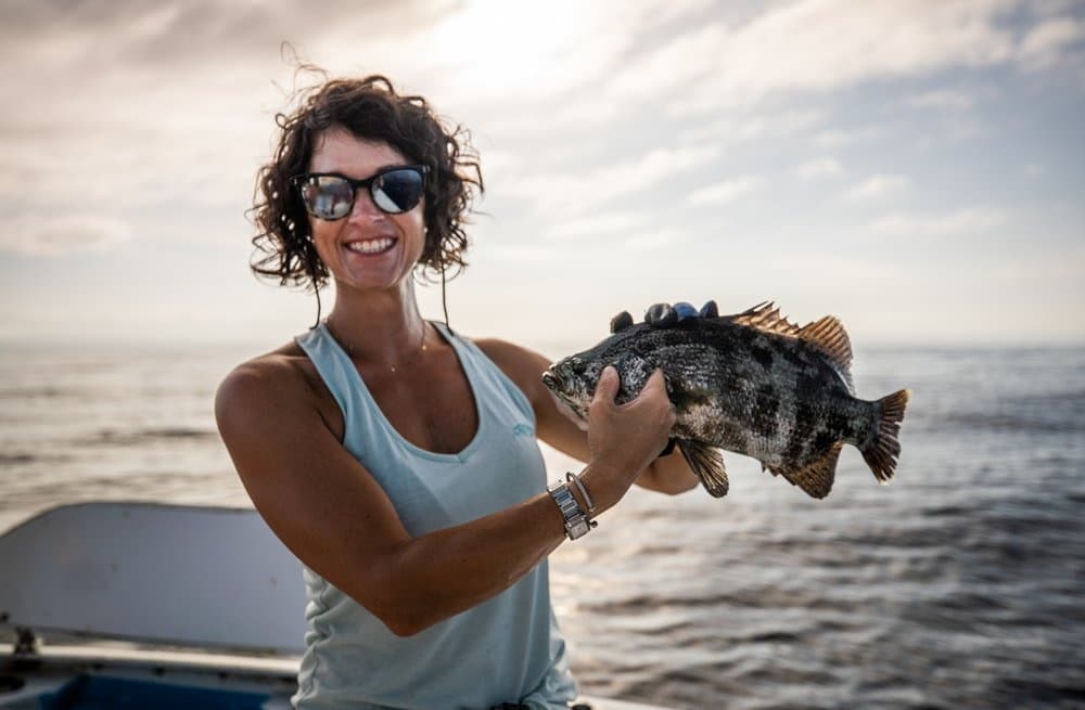 Woman angler holding a black sea bass on charter boat