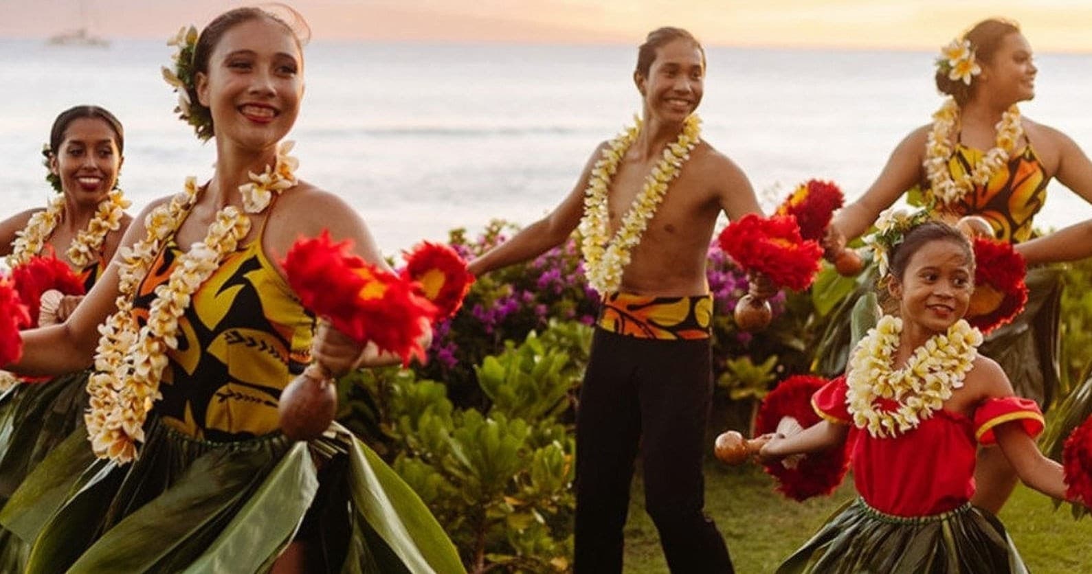 Hula dancers performing on sunset beach wearing leis and grass skirts