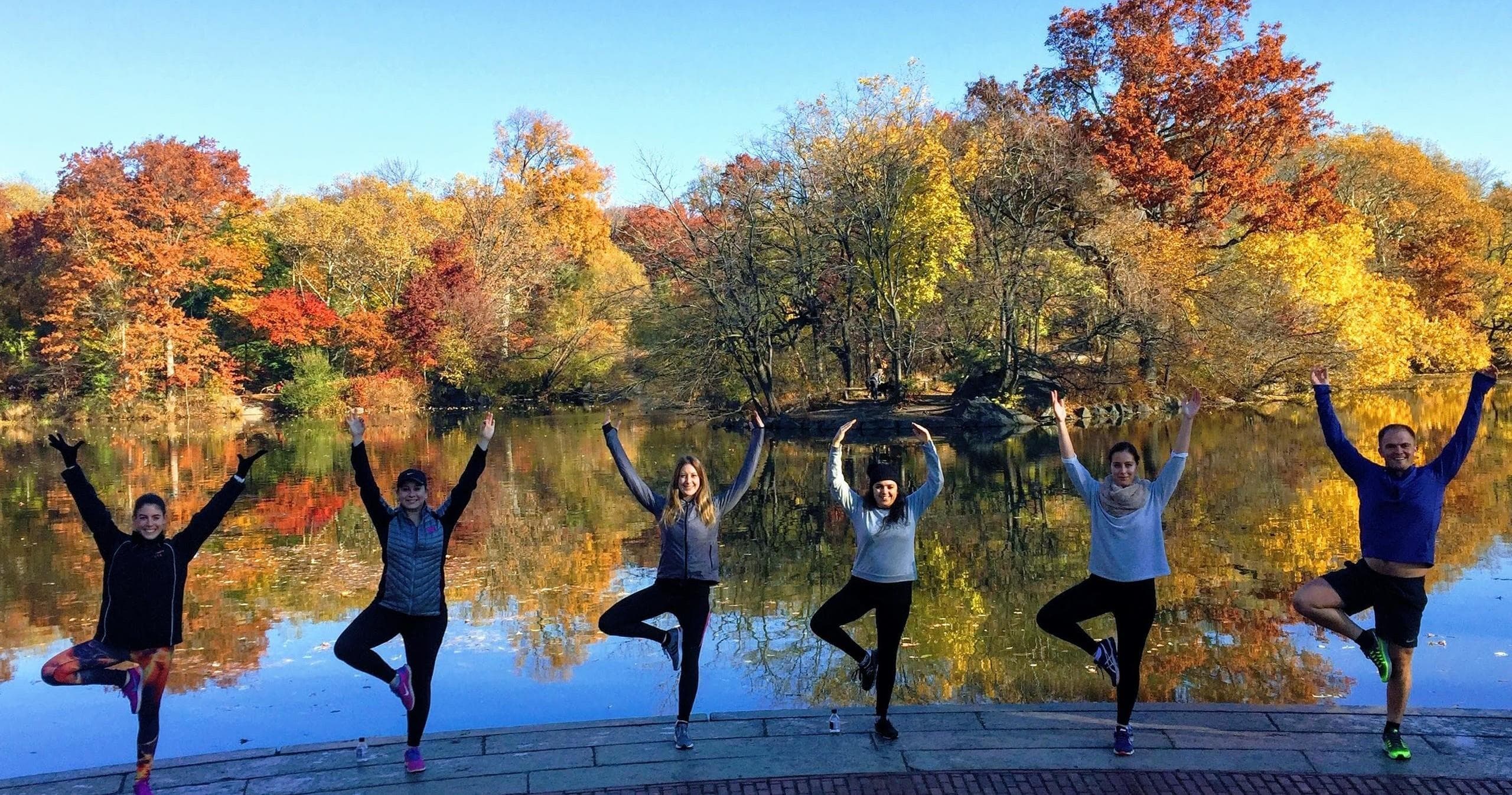 Women jumping along lake with vibrant autumn foliage