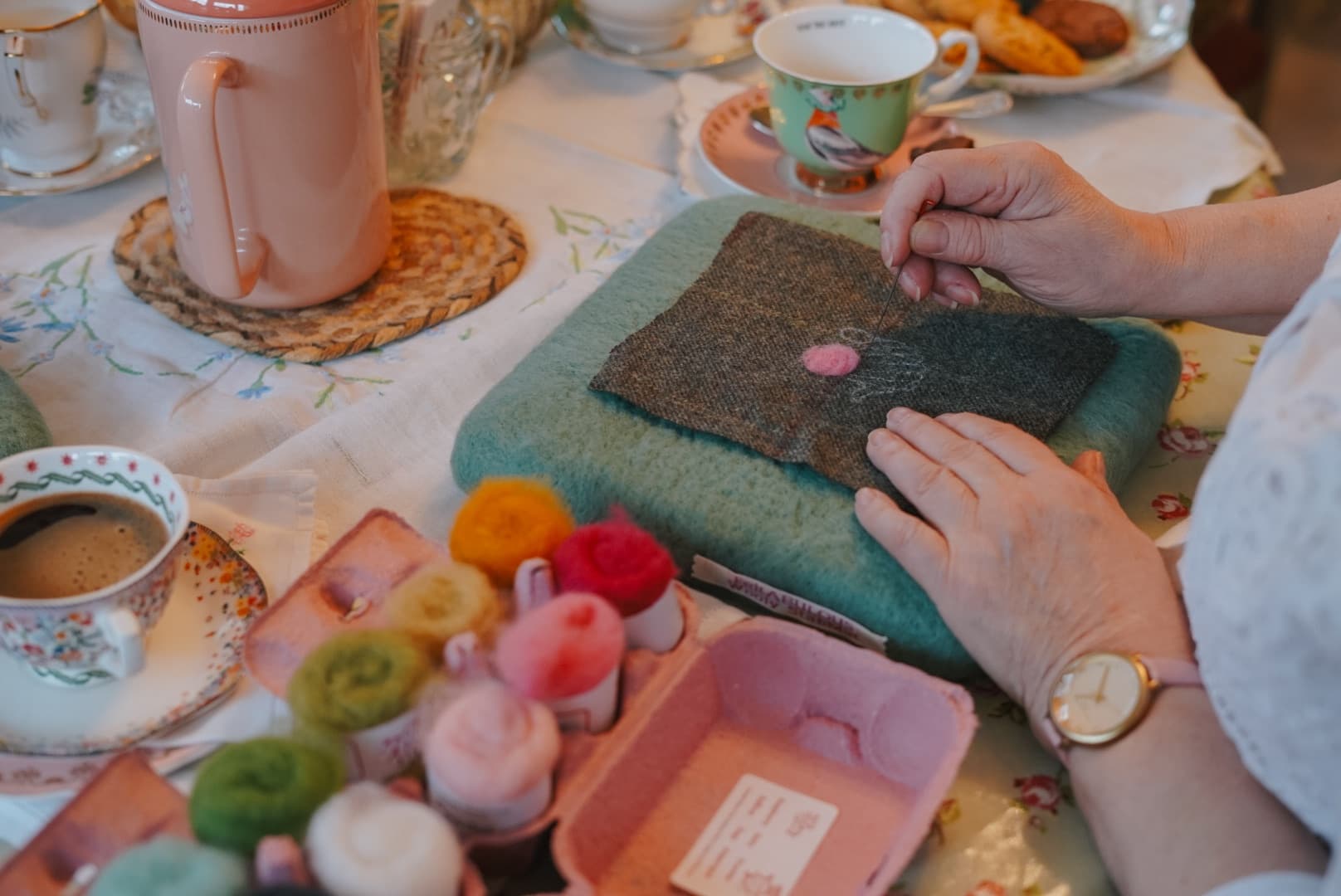 Needle felting wool at a cozy indoor craft table with tea