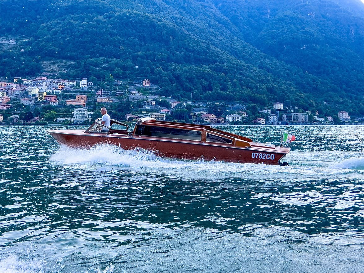 Wooden speedboat powering across alpine lake against mountain backdrop