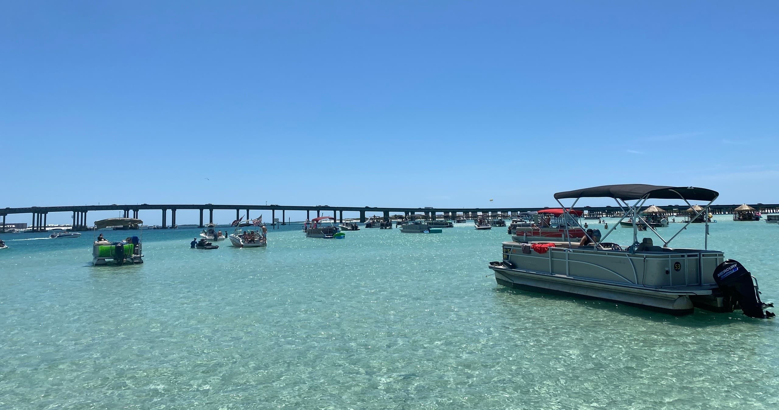 Pontoon boat anchored in crystal-clear shallow bay near bridge
