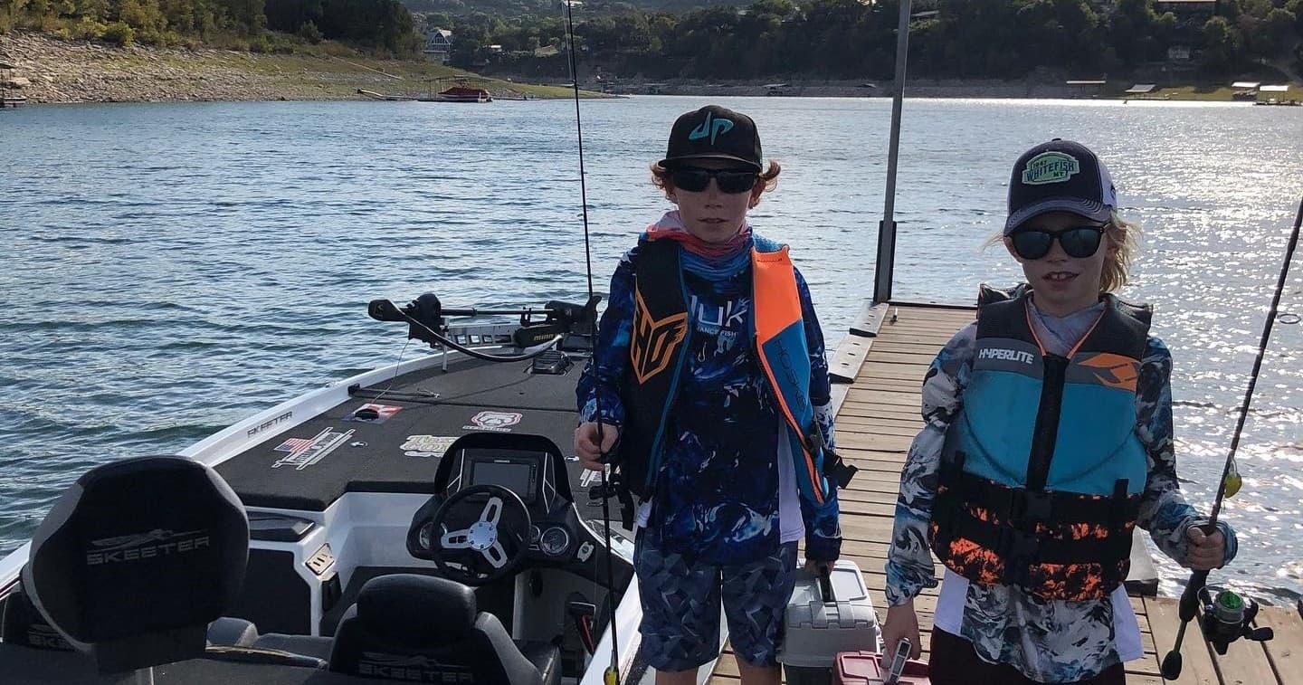 Two young anglers with rods on bass boat at lake dock
