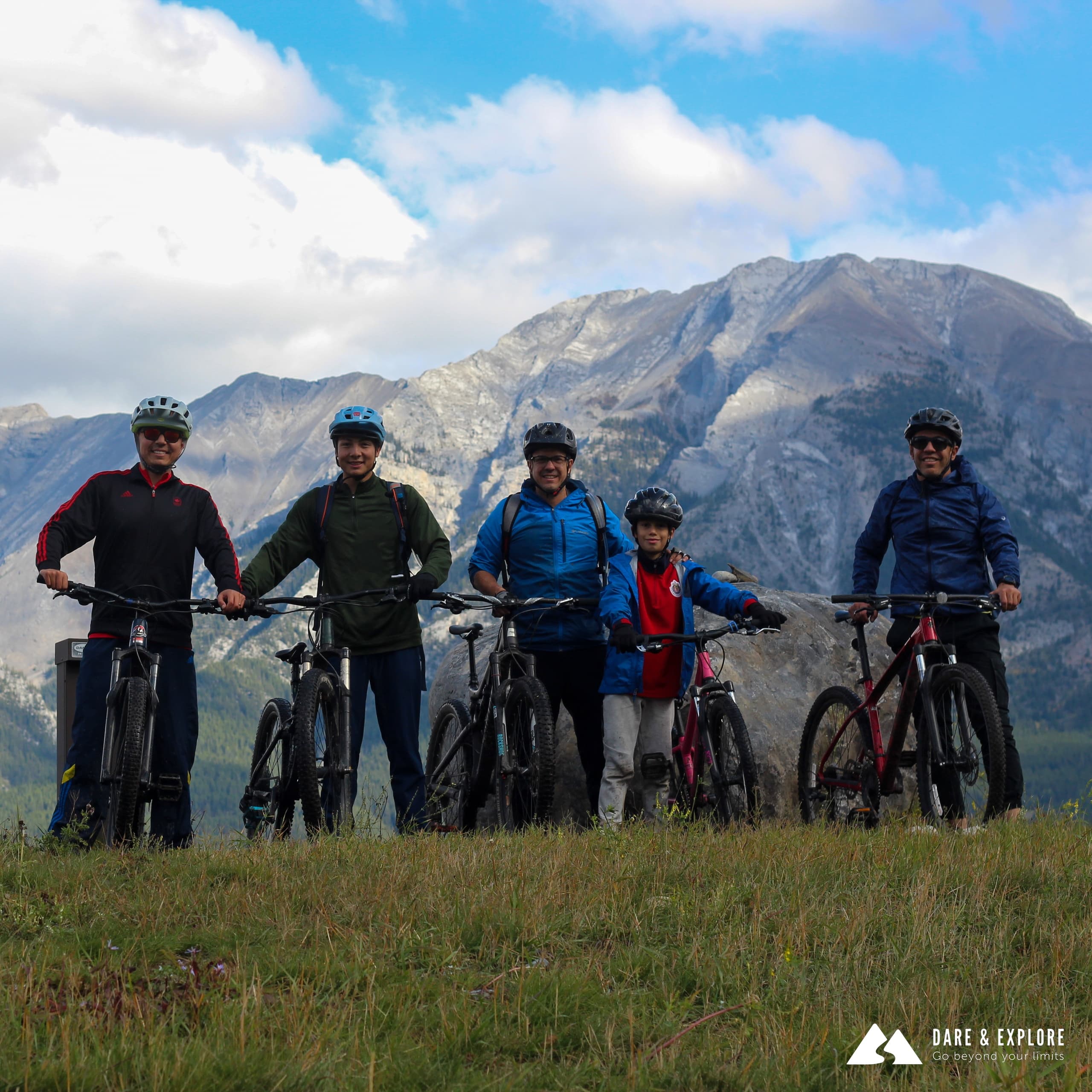 Mountain bikers posing with bikes on alpine meadow beneath peaks