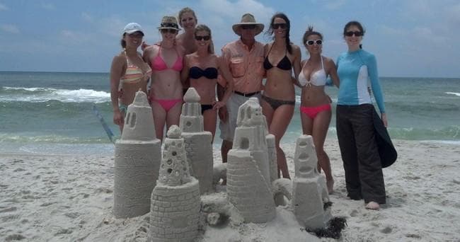 Group of friends posing with sandcastles on sunny beach