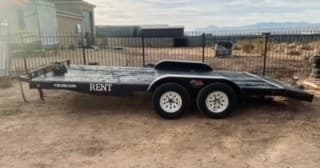 Tilt-deck car trailer parked on sandy lot ready for vehicle transport
