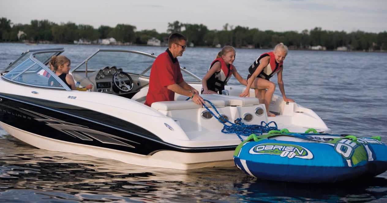 Family prepping inflatable tube behind motorboat on lake