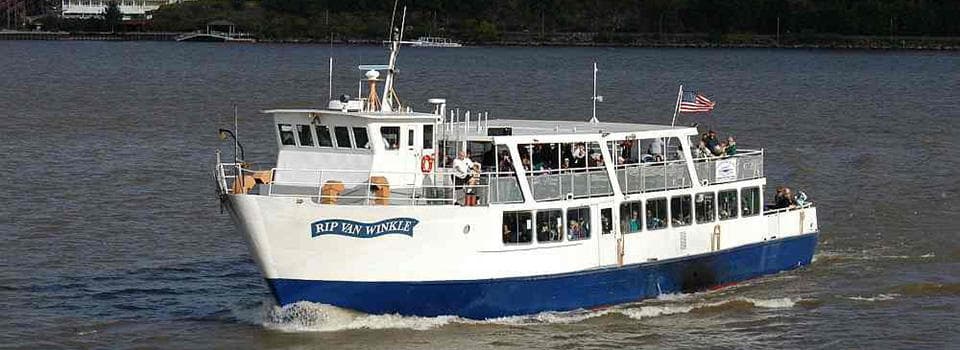 River cruise boat cutting through Hudson River waters near shoreline