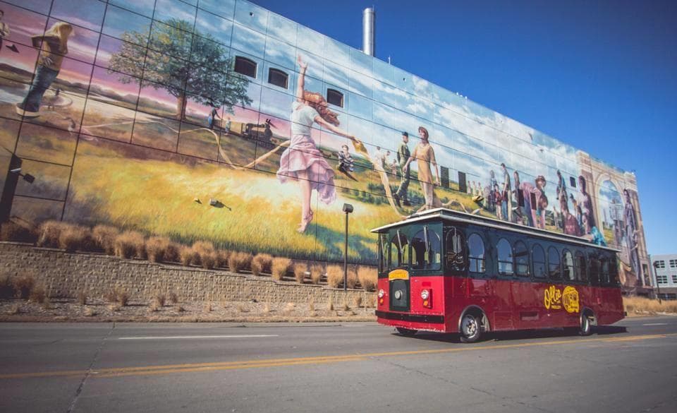 Red trolley passing mural on sunny street showing city tour