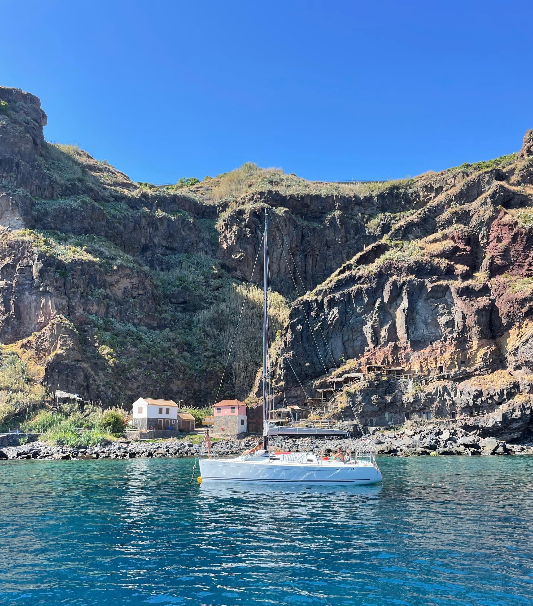 Sailboat anchored beside dramatic volcanic cliffs in clear sea