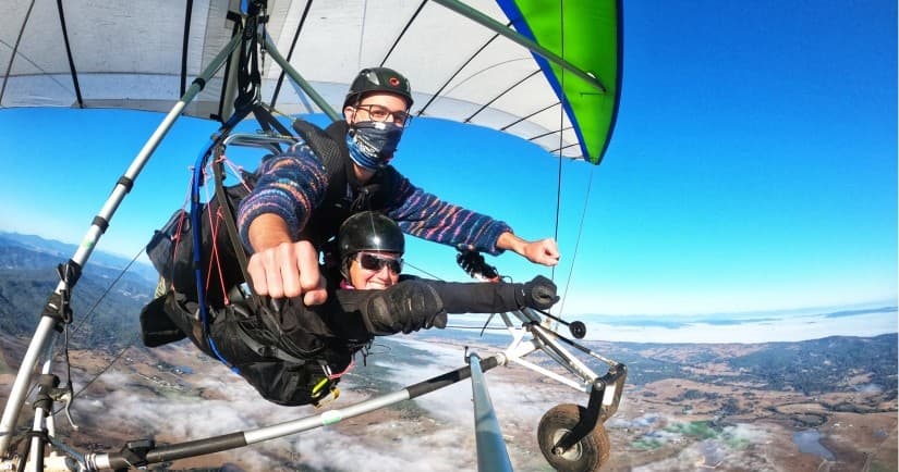Tandem hang gliding above coastal hills and valley, airborne experience