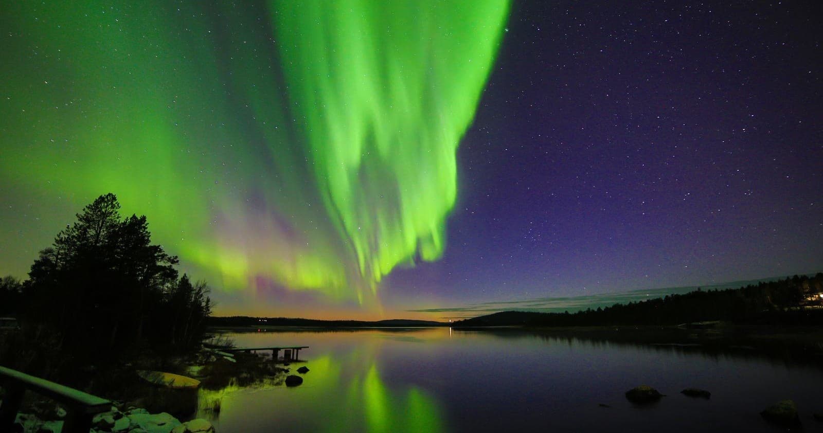 Dramatic northern lights above a lakeshore with silhouetted trees