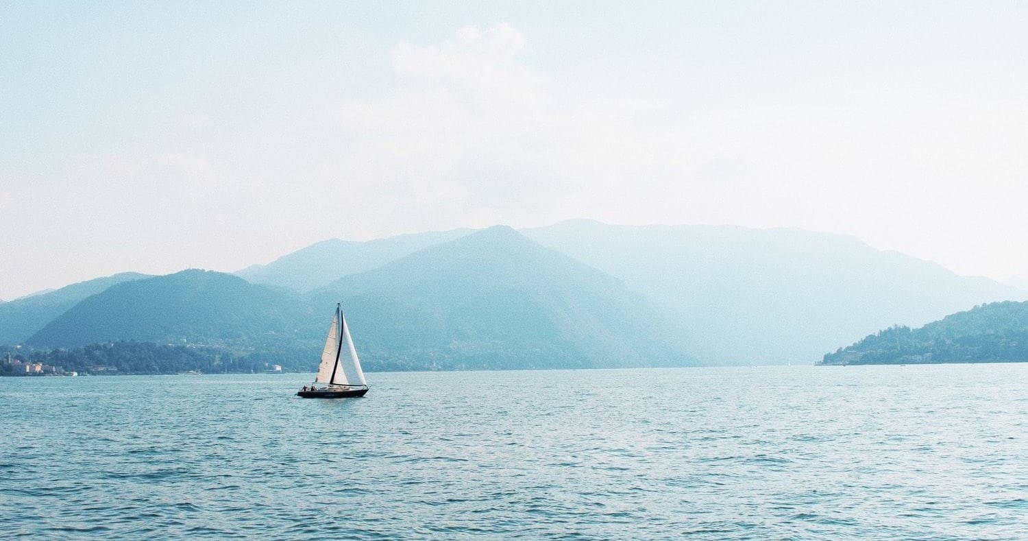 Sailboat cruising on calm alpine lake with misty mountains