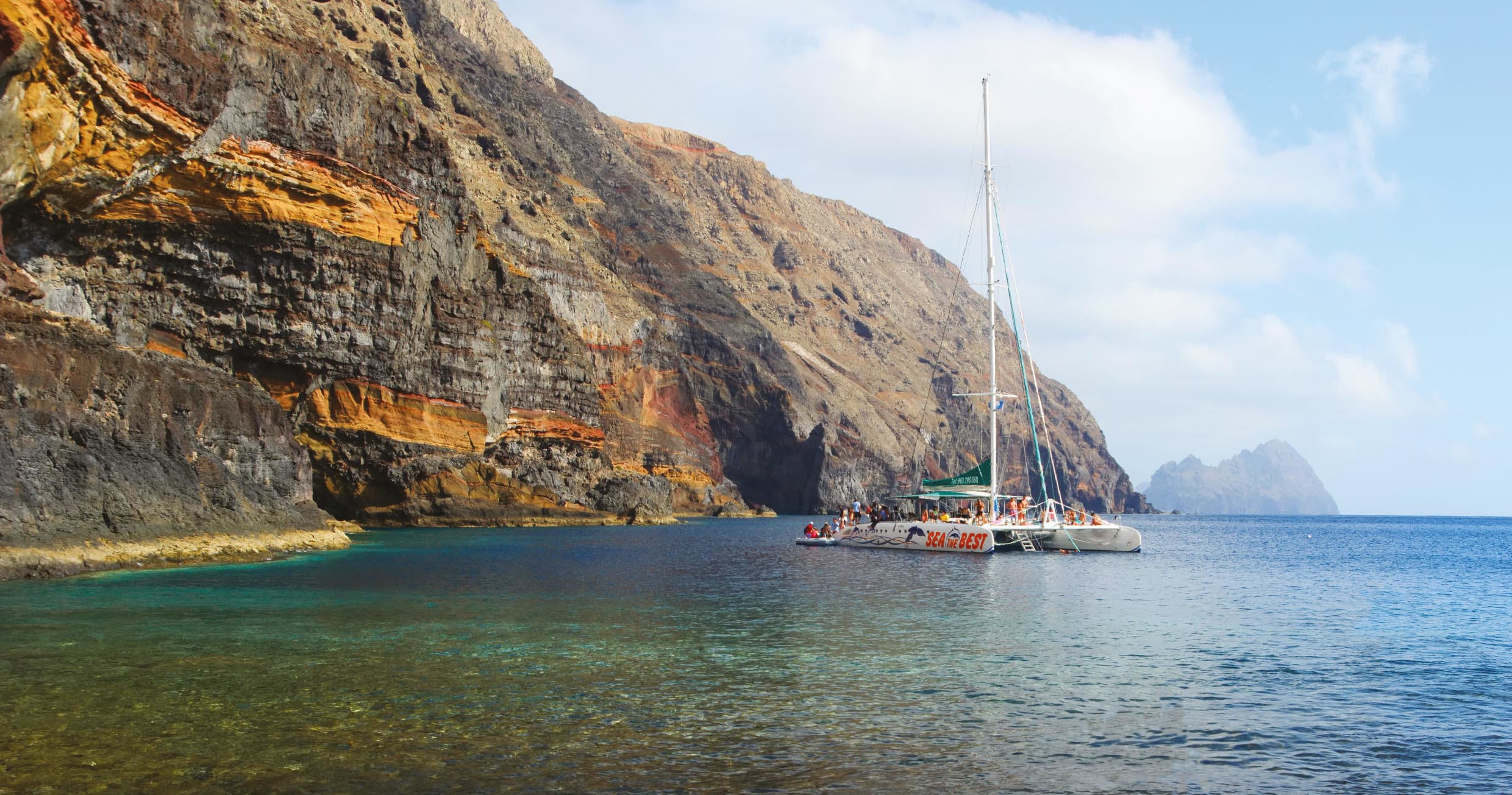 Sailboat anchored in crystal bay below steep island cliffs