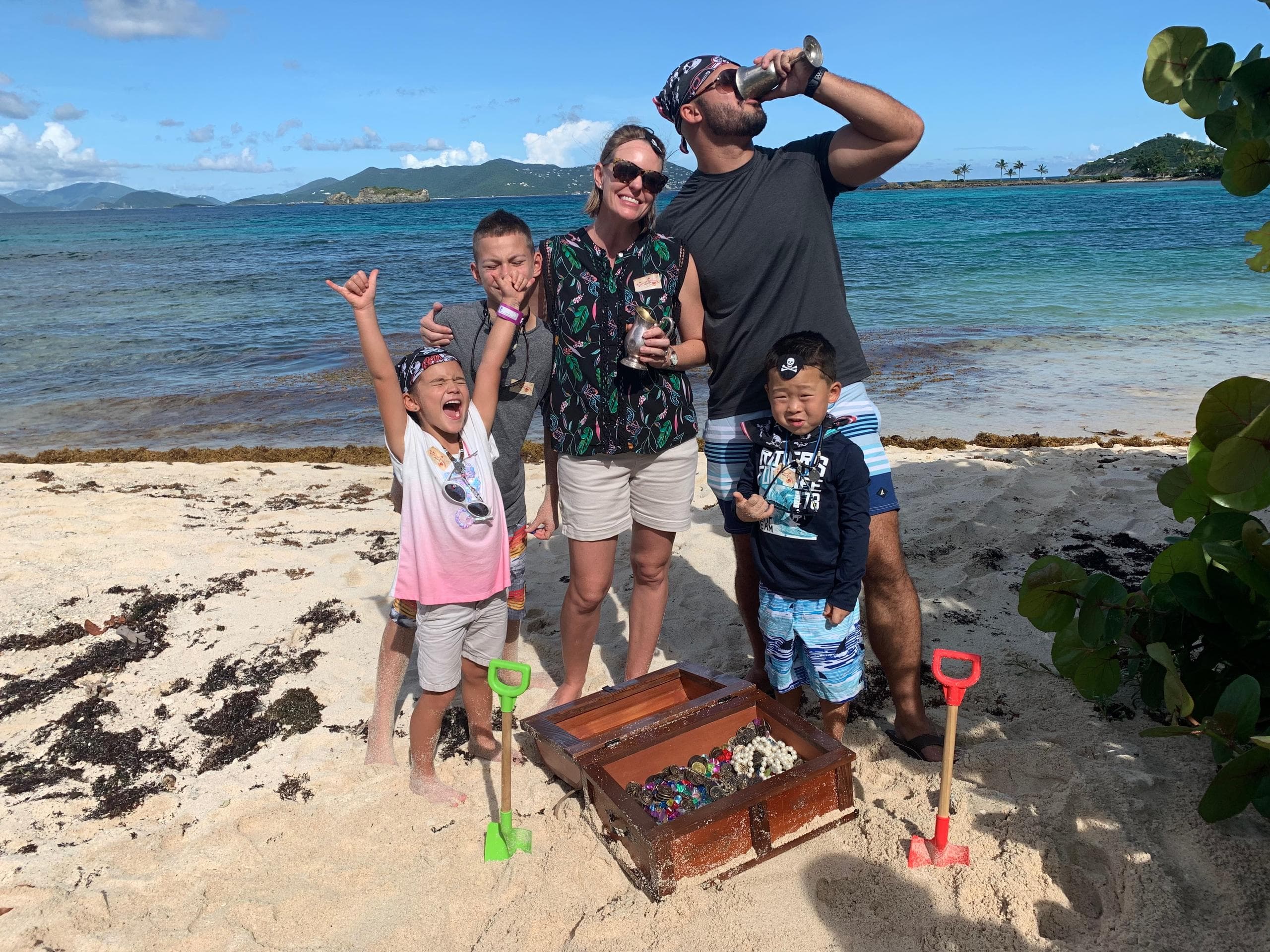 Family finding treasure chest on sandy beach near tropical lagoon