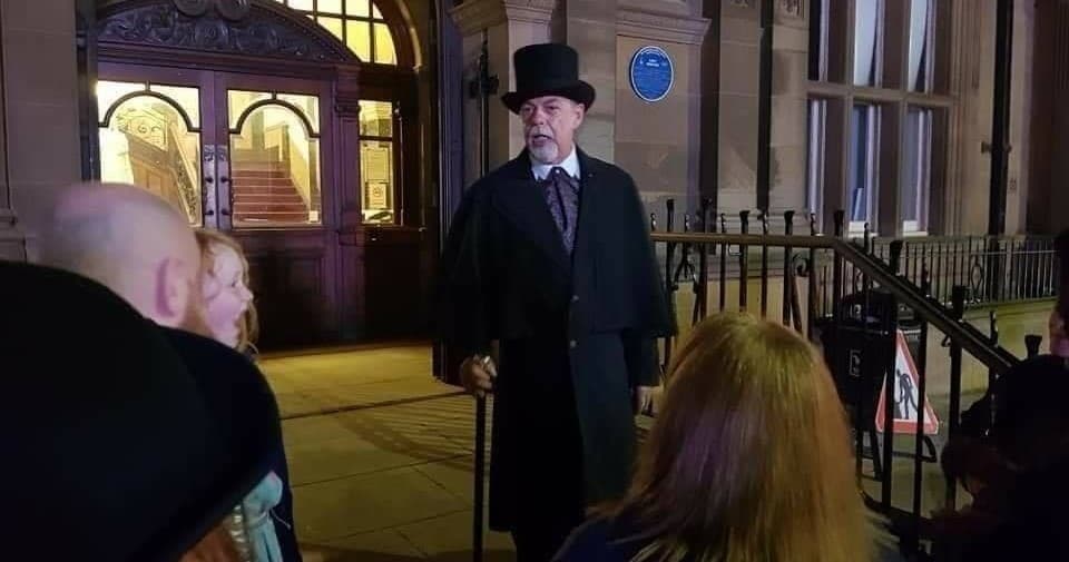 Victorian ghost tour host speaking to night-time crowd outside historic theater