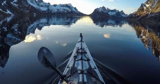 Kayak bow cutting through mirrored fjord waters at sunrise