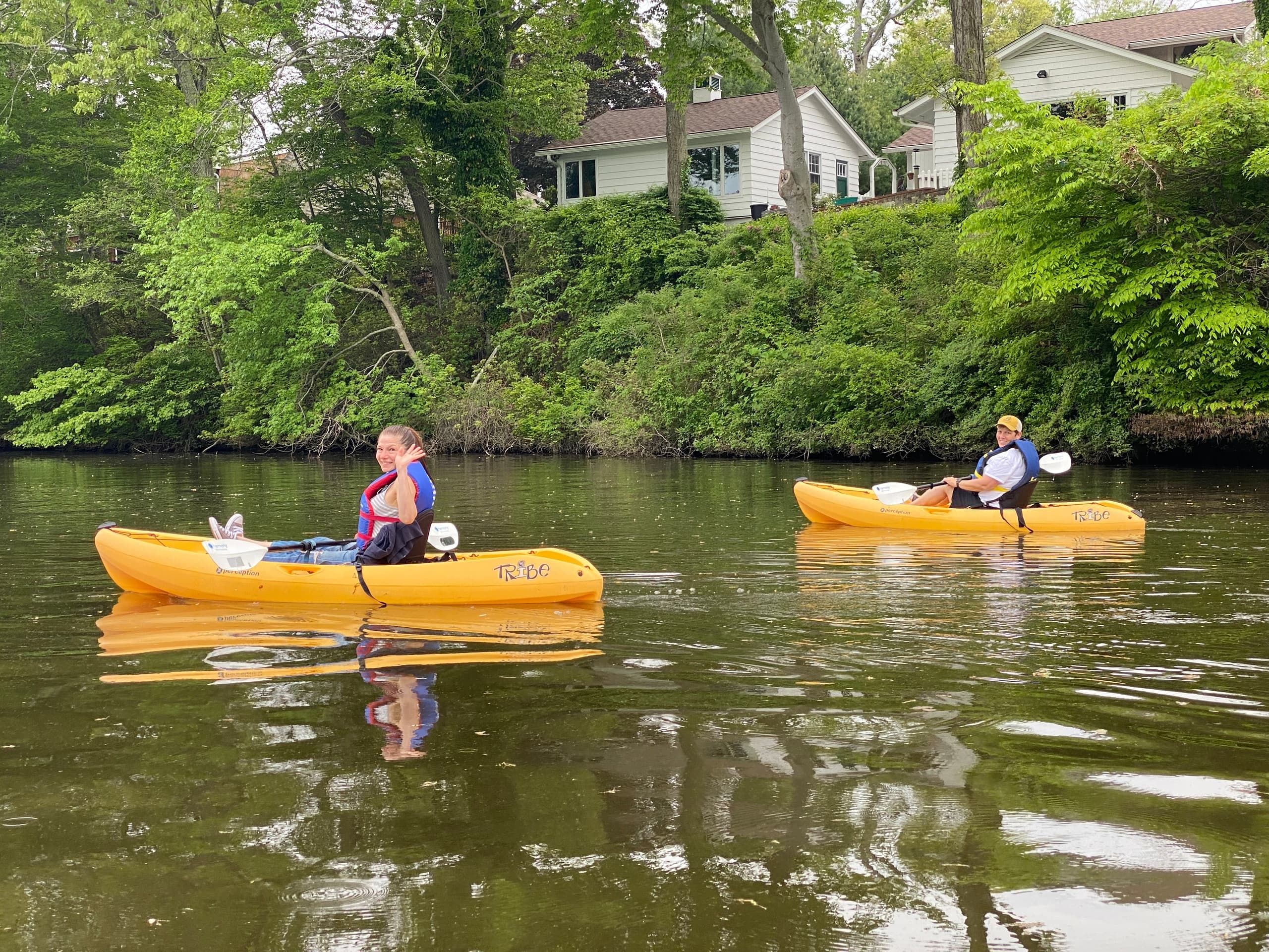 Solo kayaker gliding past riverbank houses on tranquil water
