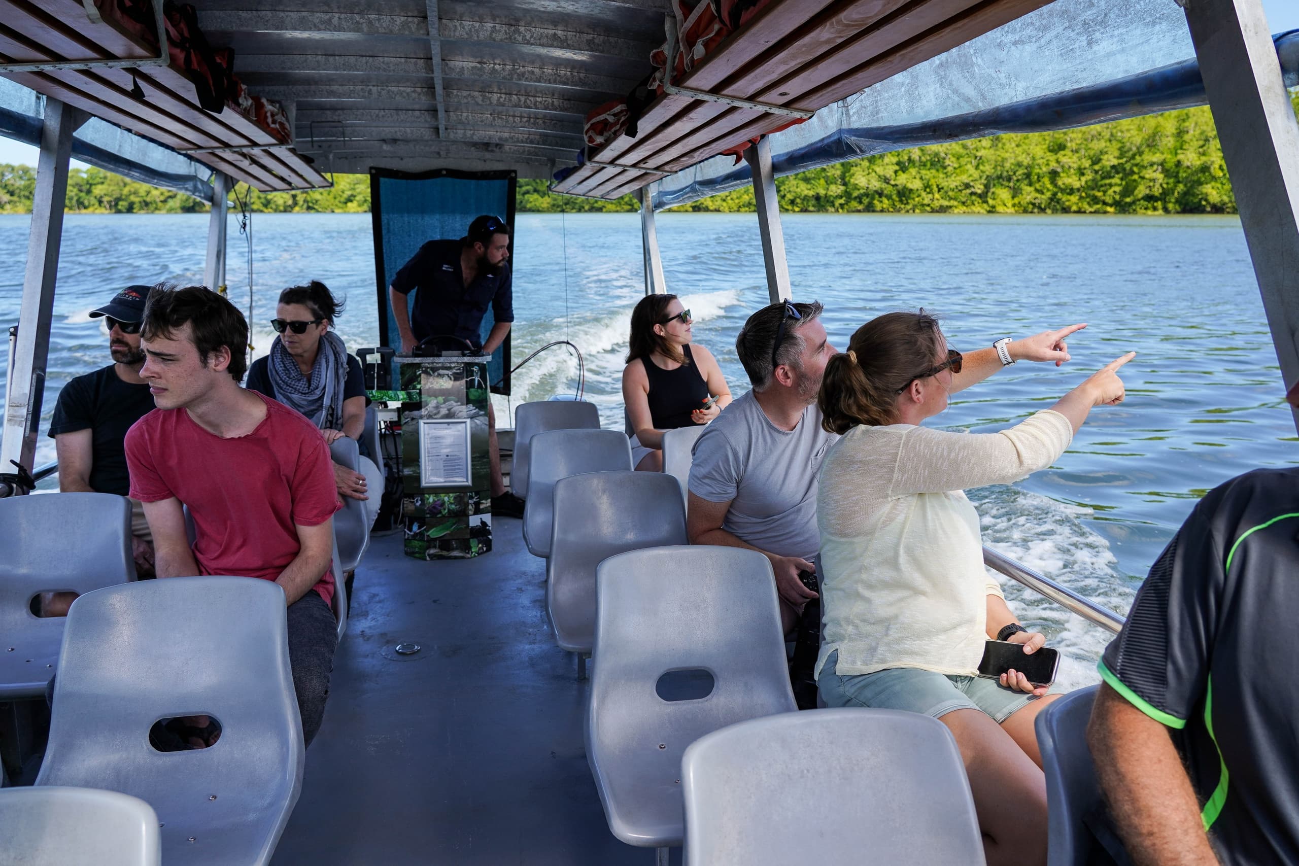 Passengers on open boat pointing at river scenery on eco cruise