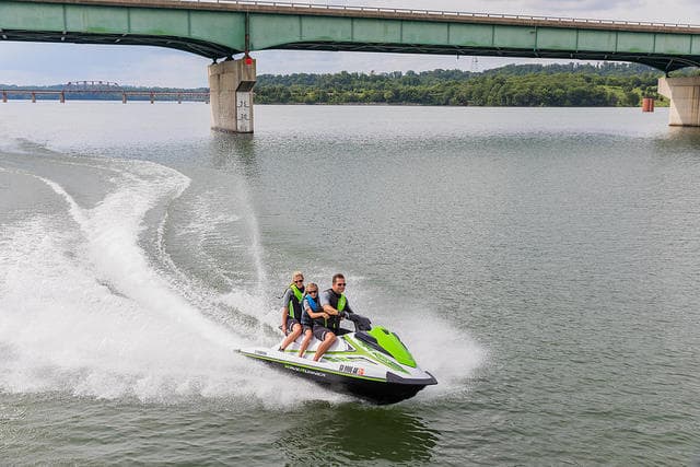 Two riders on jet ski speeding under bridge across calm river