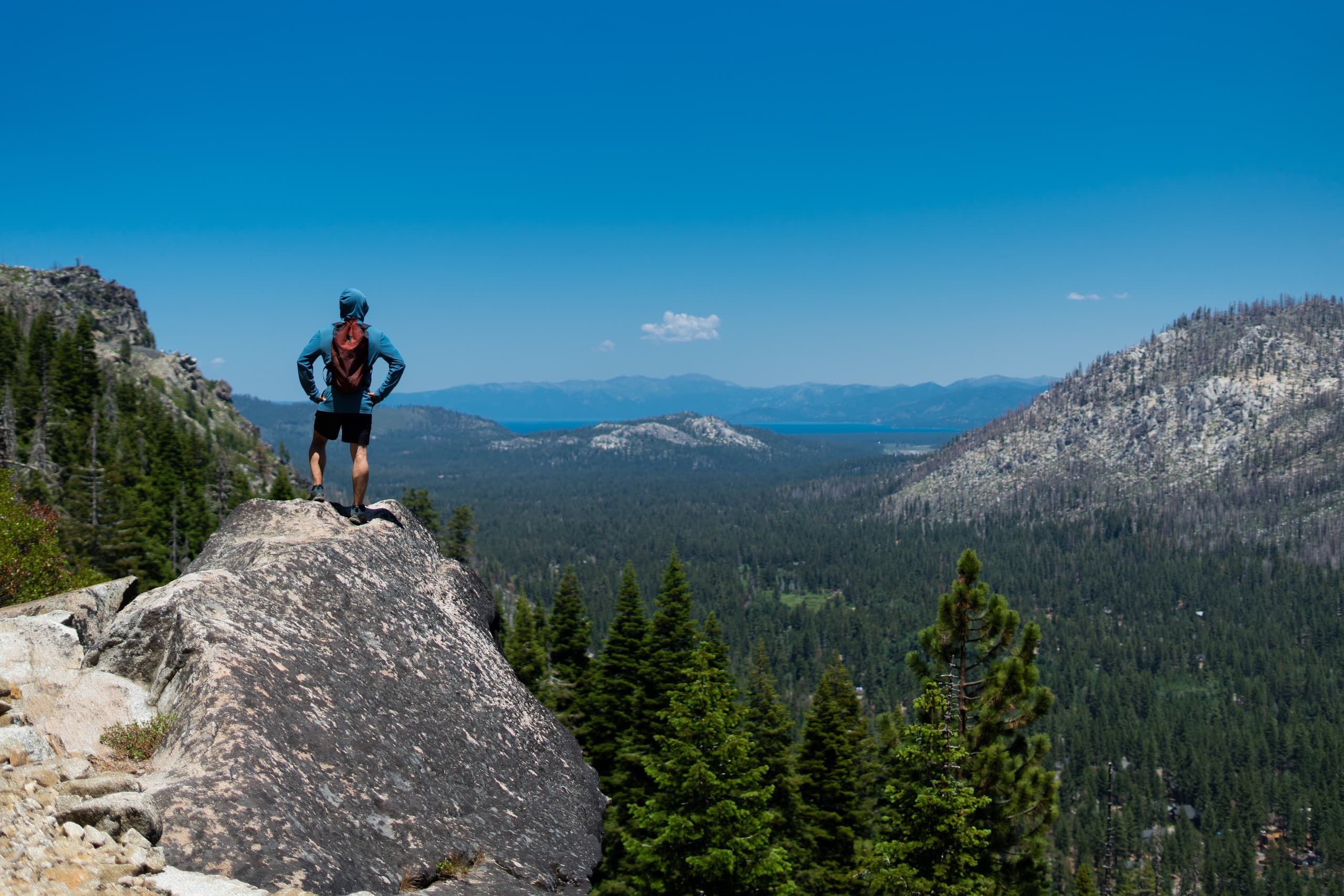 Hiker standing on granite overlook above Tahoe forest valley