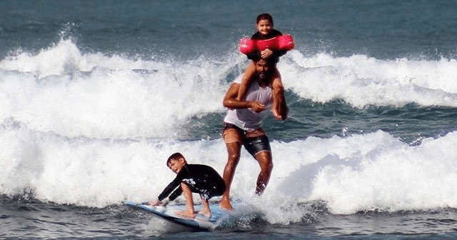 Group doing surfing acrobatics with person lifted atop board in Hawaii