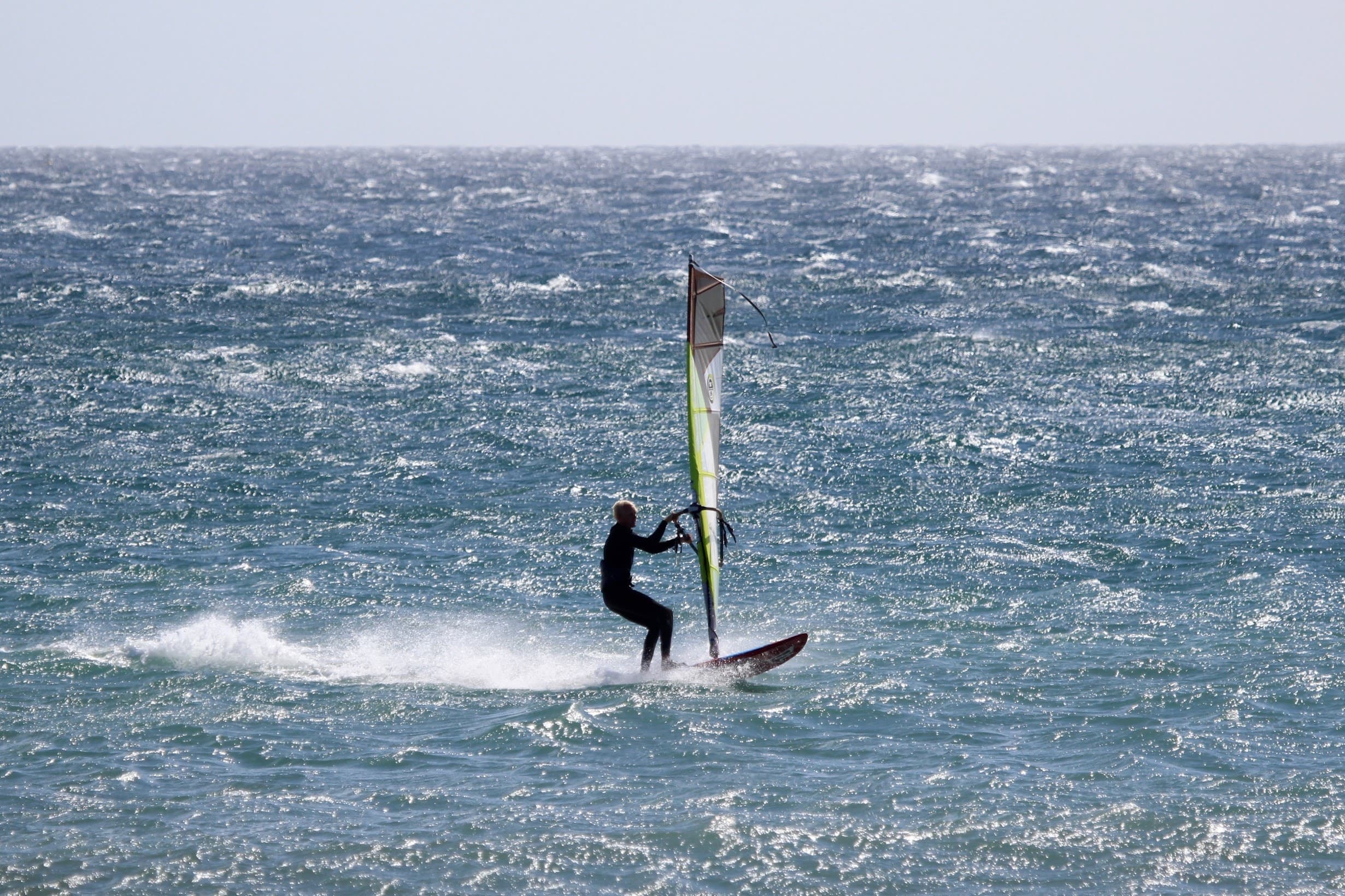 Windsurfer carving across open ocean with clear sky, Gran Canaria