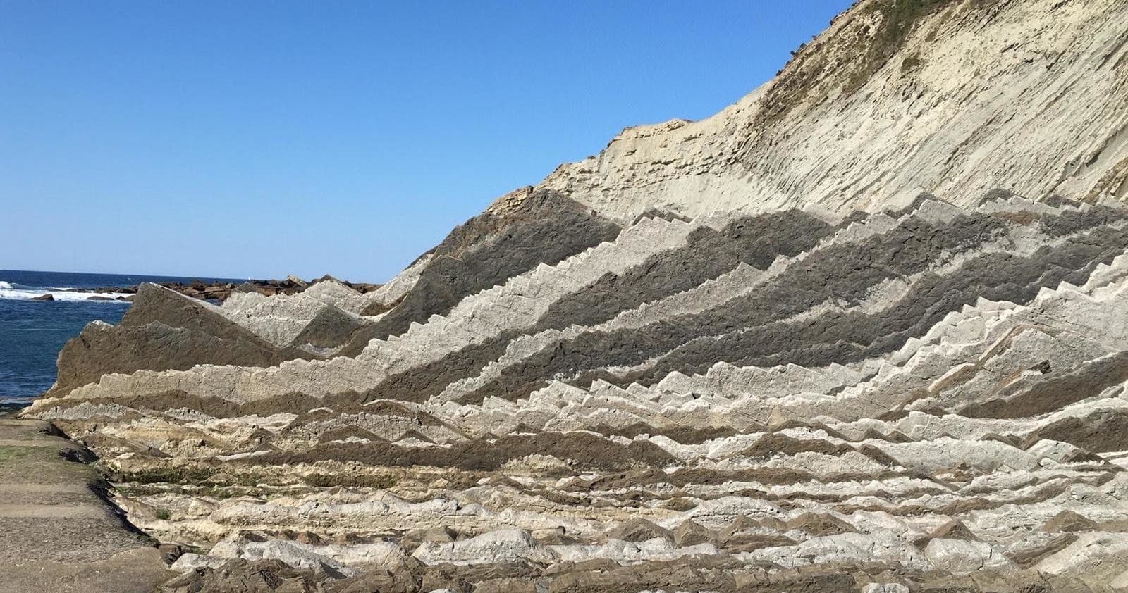 Folded rock strata along rugged seaside cliffs, coastal geology view
