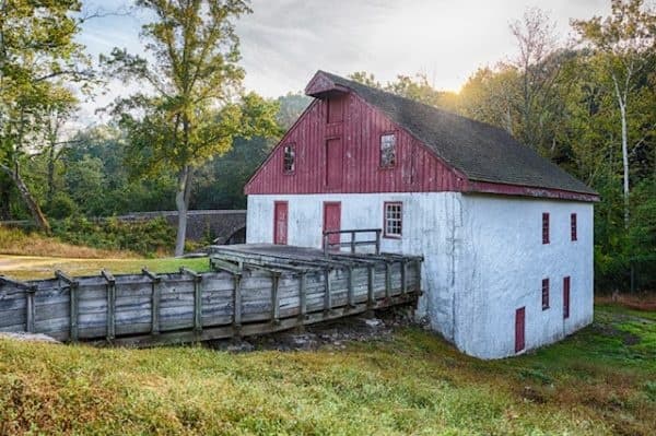 Historic red mill and wooden bridge beside grassy meadow