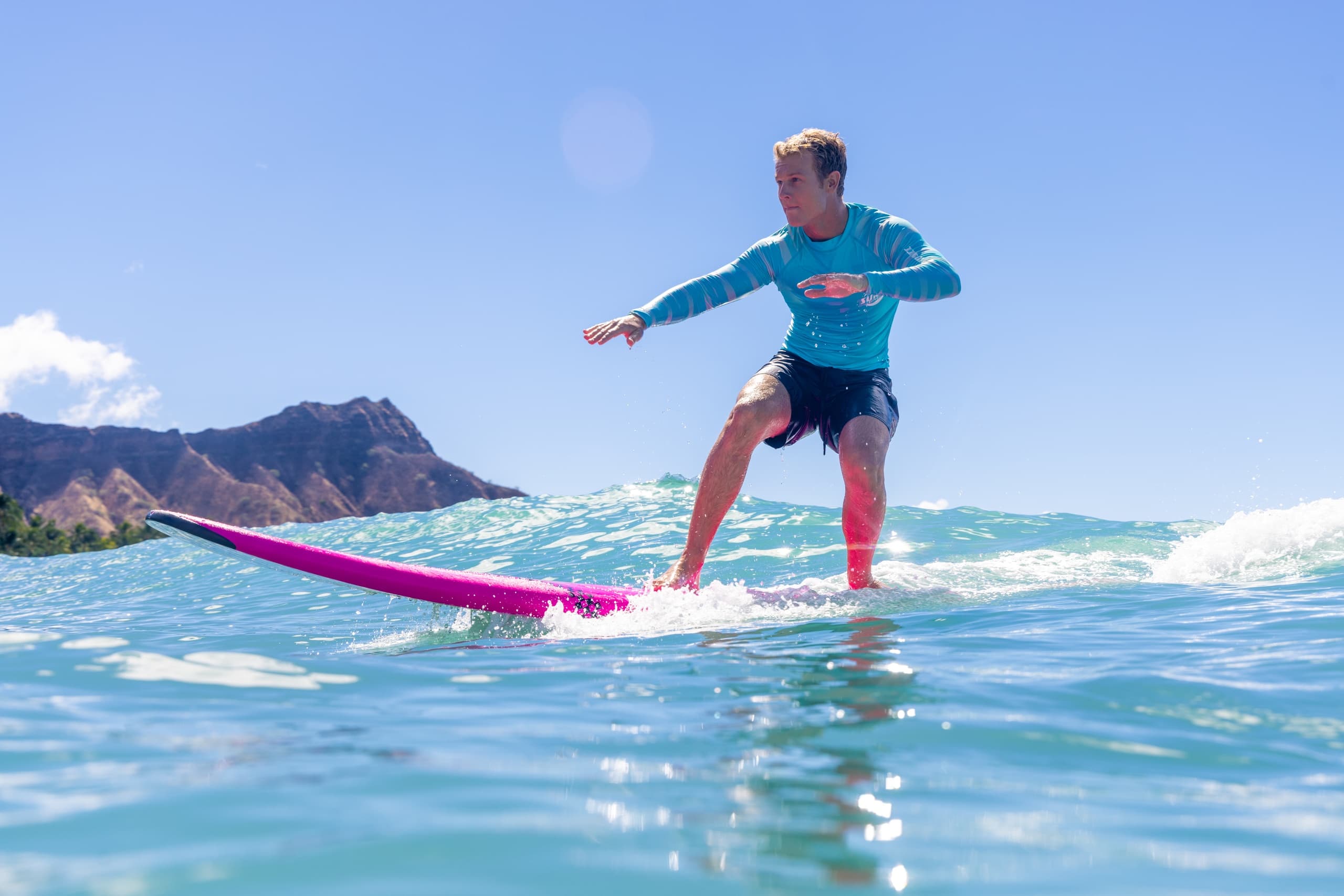 Young surfer riding small wave toward Diamond Head at Waikiki beach
