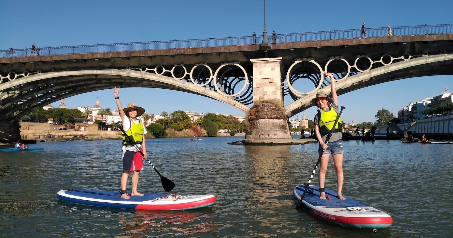 Paddleboarders cruising under historic Sevillian bridge