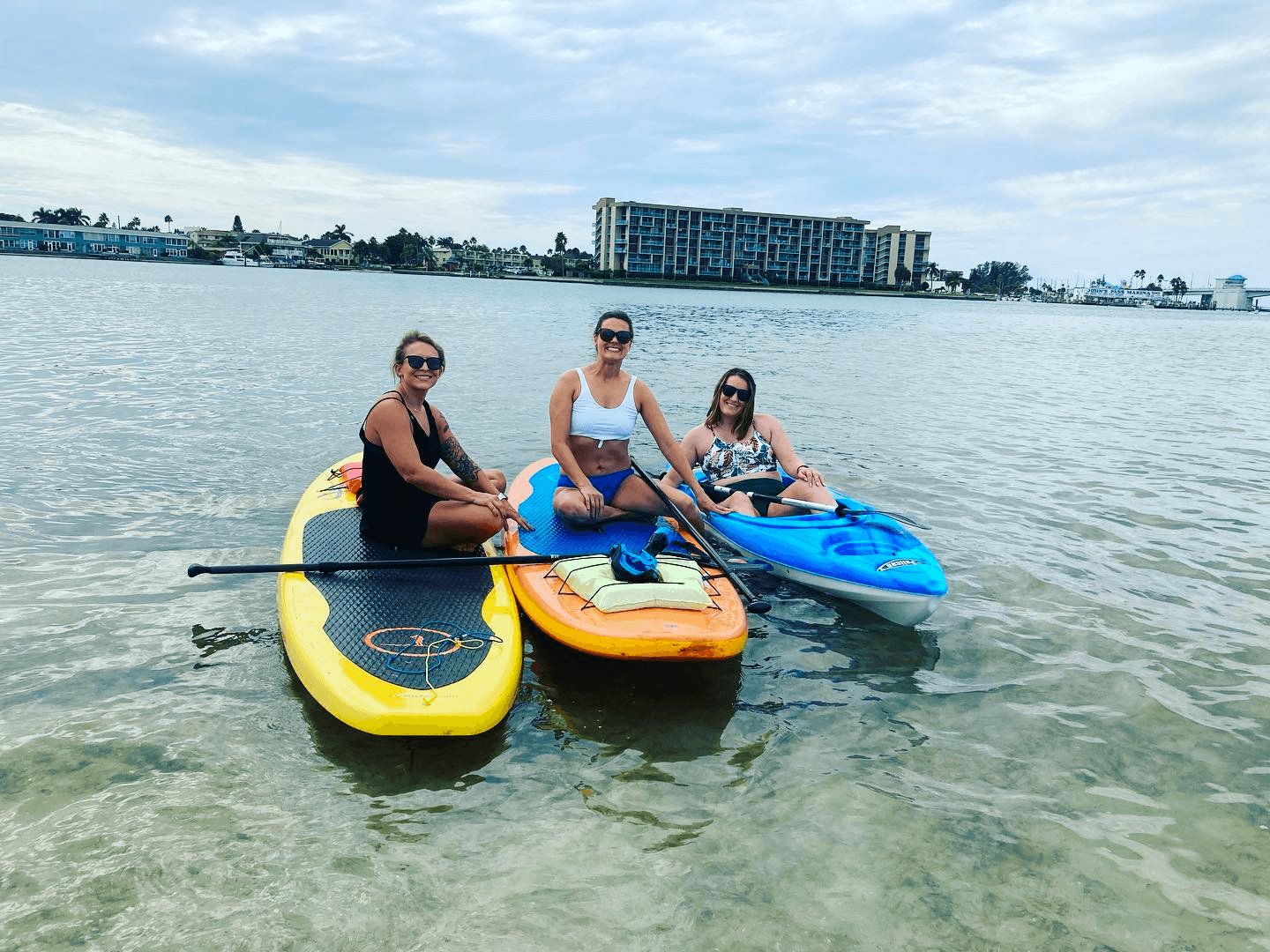 Three paddlers on kayaks and SUPs in shallow coastal water