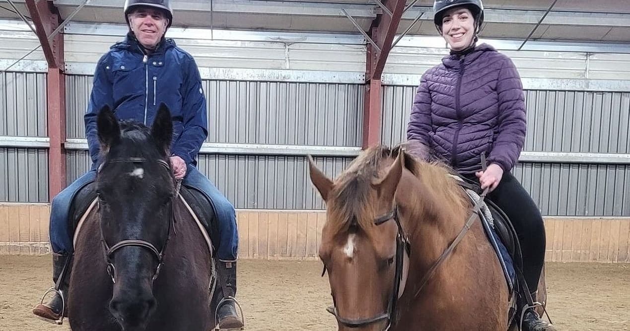 Two riders on lesson horses inside an indoor arena