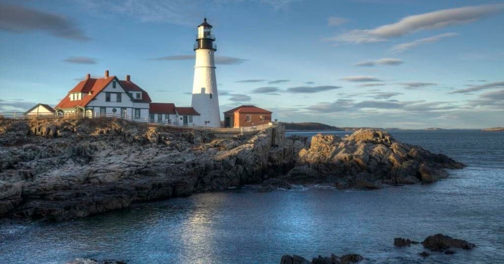 Lighthouse on rocky coastal Maine shoreline at golden hour