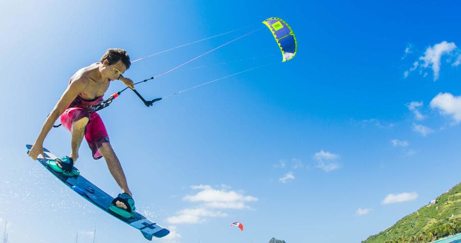 Kitesurfer airborne over blue ocean with coastal backdrop