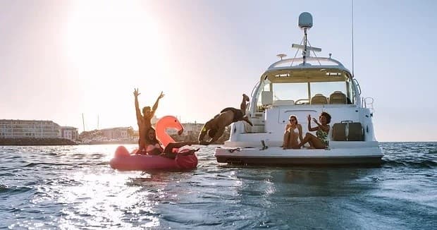 Friends tubing and relaxing beside anchored yacht in bay