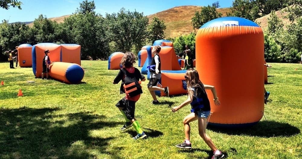 Children running in outdoor inflatable nerf arena on grassy park