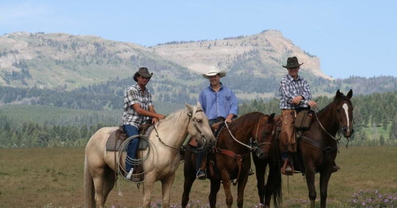 Three horseback riders on prairie with mountain backdrop in Yellowstone