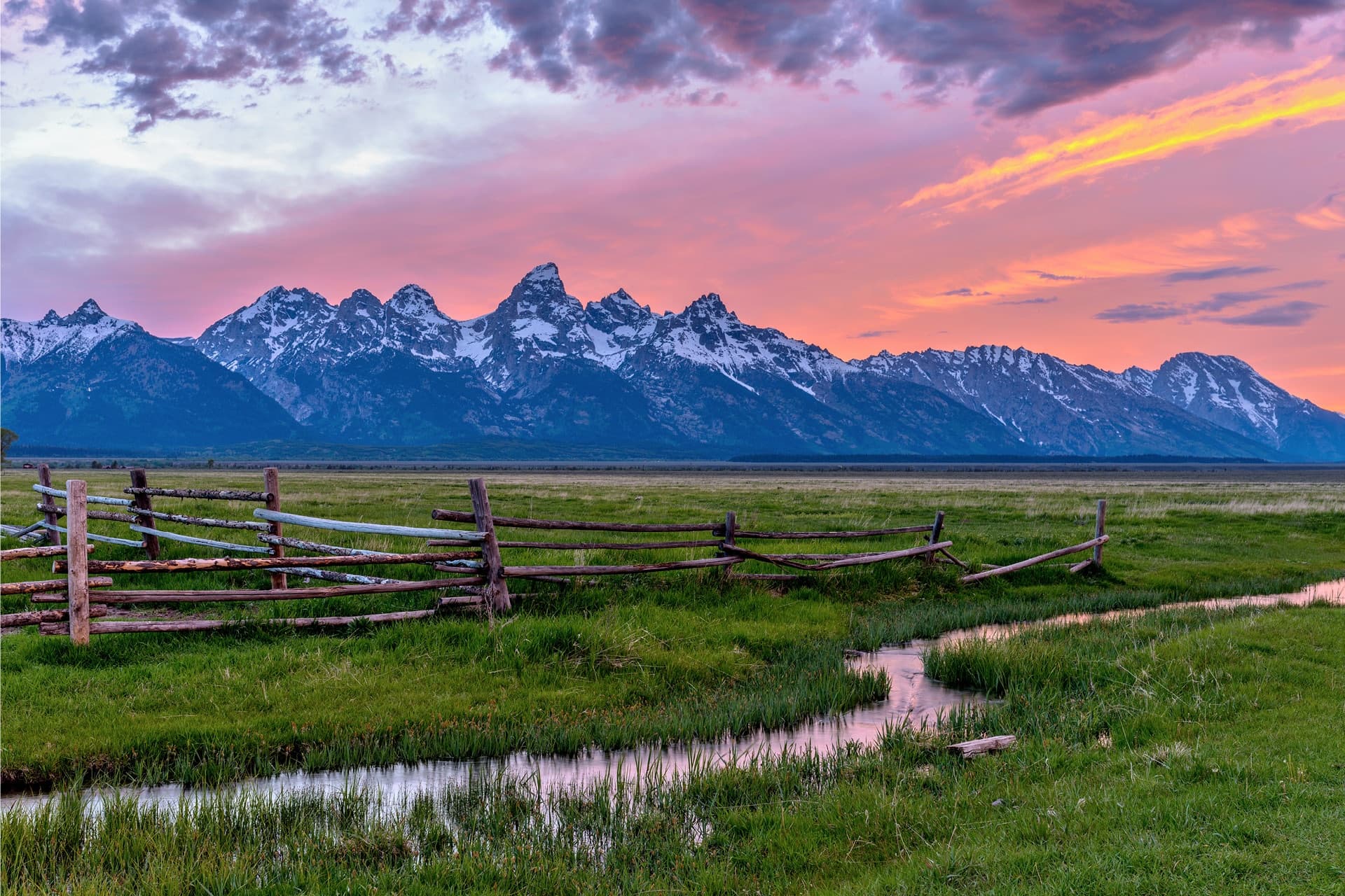 Ranch fence meadow with winding stream and mountain panorama