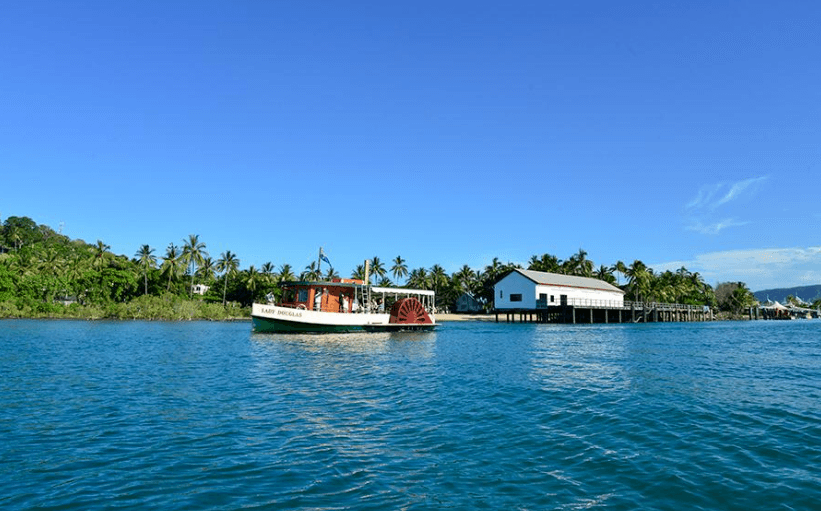 Small riverboat passing coastal village waterfront under clear blue sky