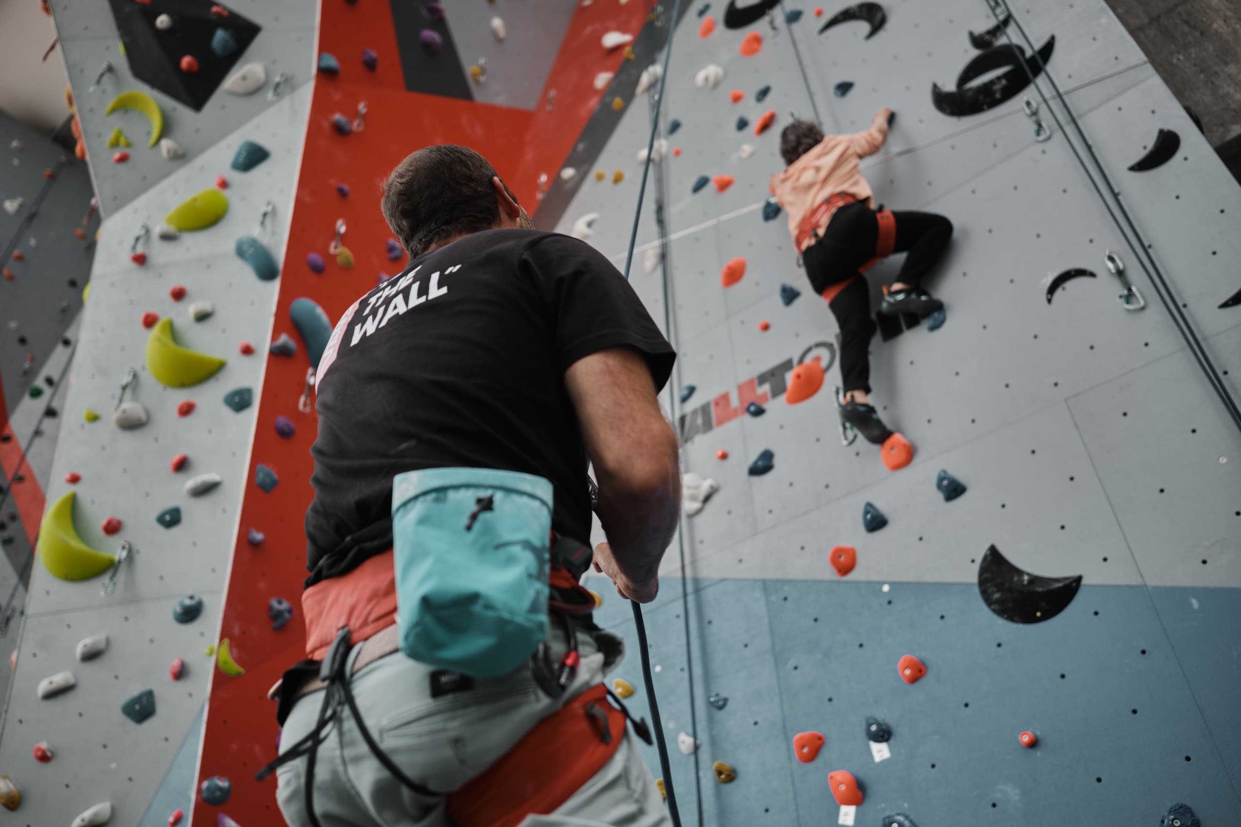 Indoor sport climber scaling colorful wall while partner belays