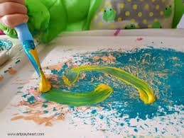 Child painting bright swirls with brush on paper at table