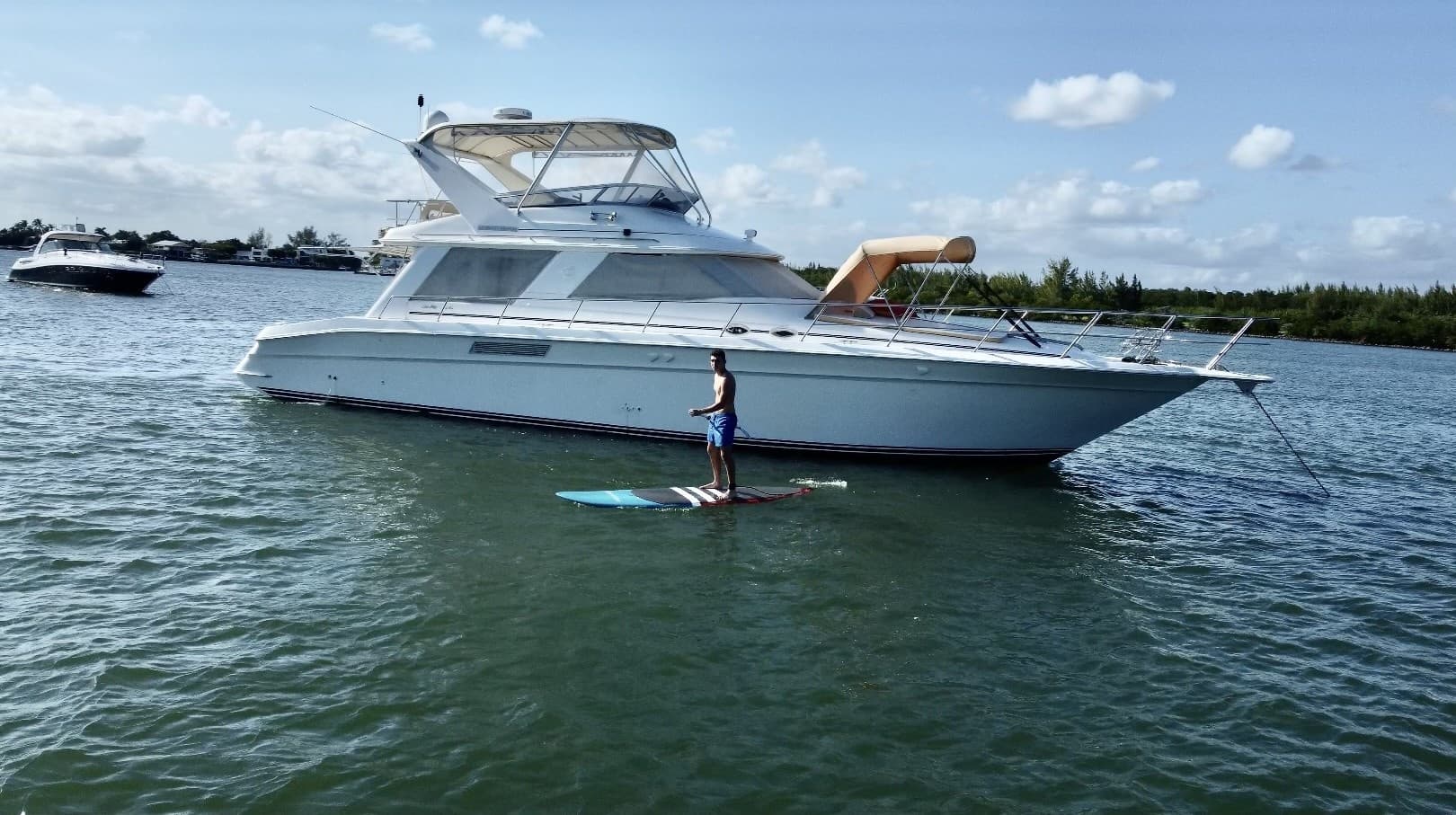 Yacht anchored with paddleboarder standing in coastal waters