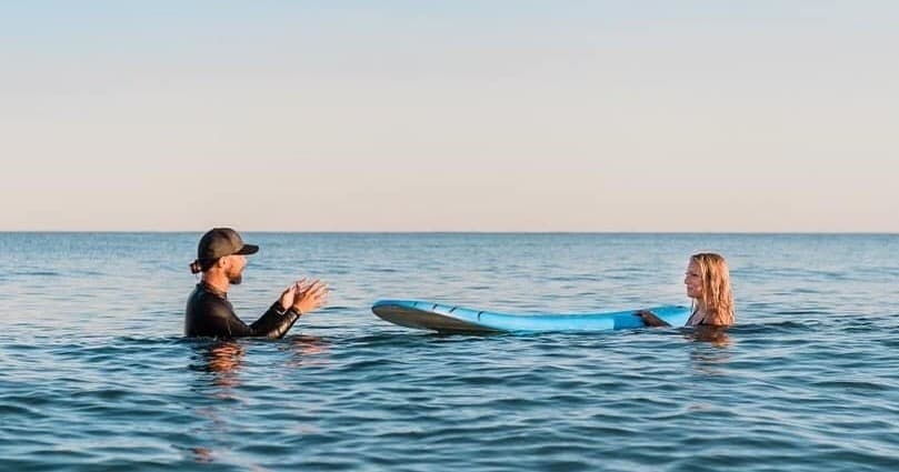 Instructor coaching beginner on surfboard in calm open ocean waters