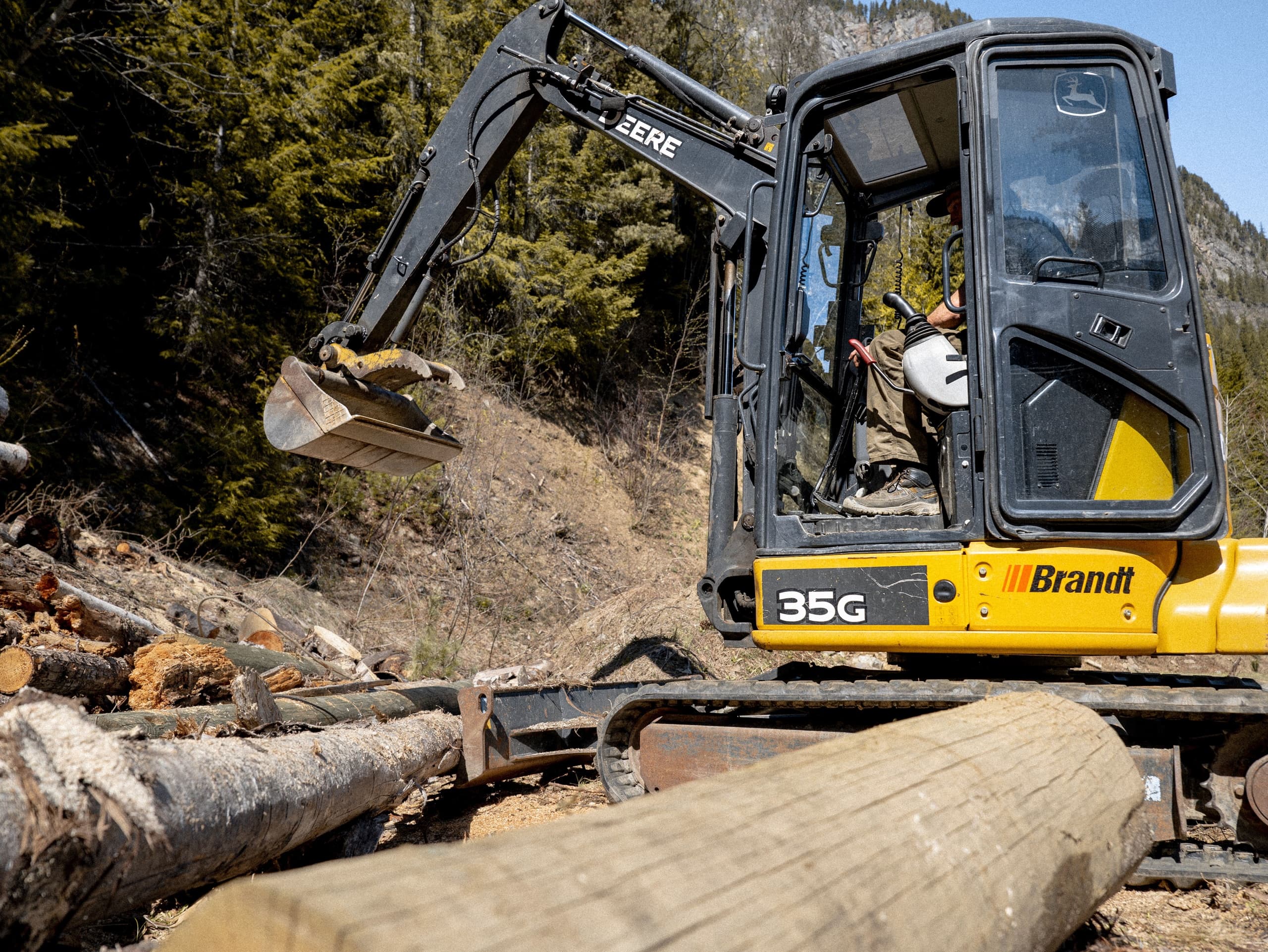 Compact excavator working among felled logs in wooded hillside