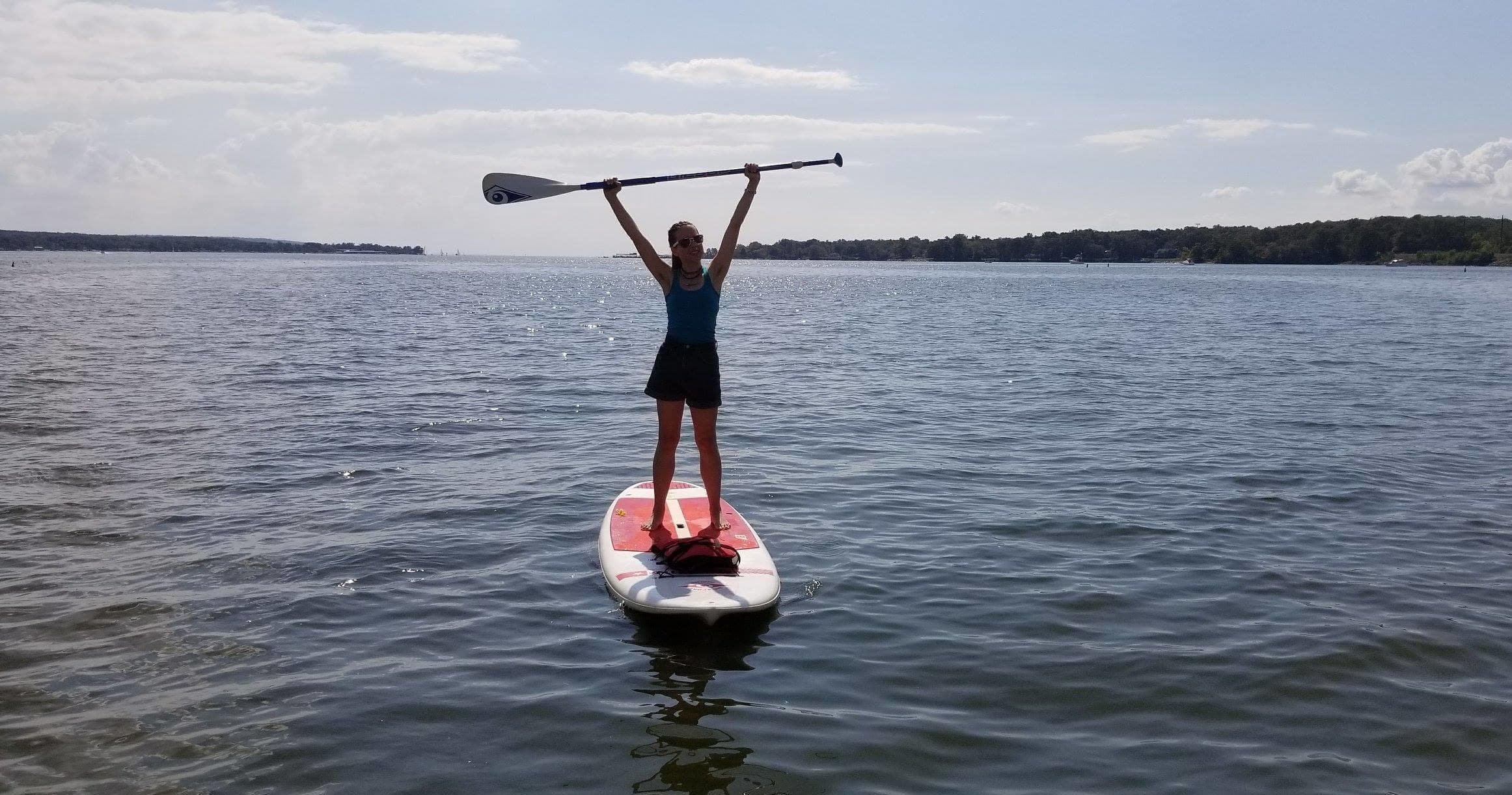 Stand-up paddleboarder celebrating on open lake, arms raised